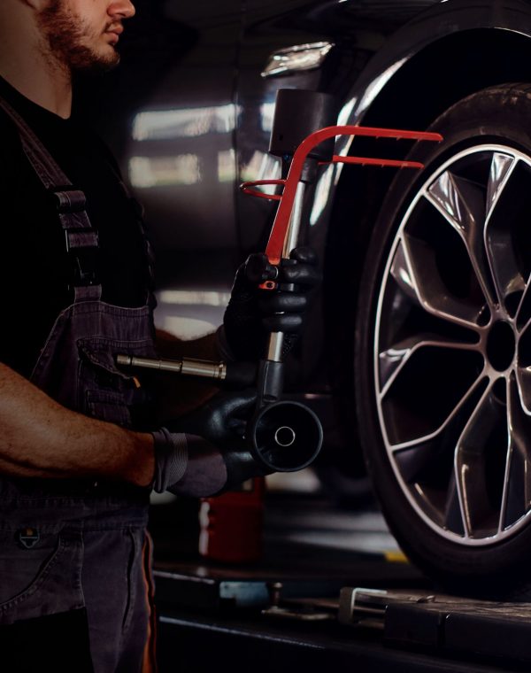 Muscular man is fixing car's wheel with special tool at auto service.