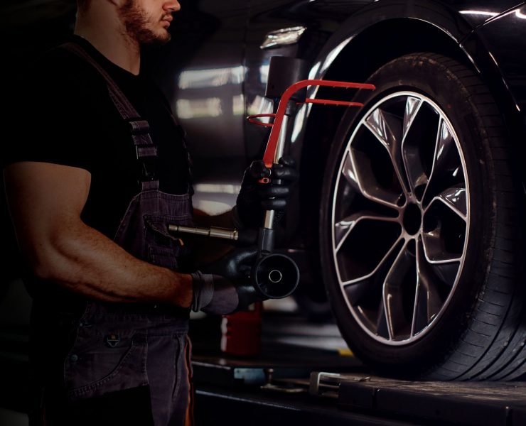 Muscular man is fixing car's wheel with special tool at auto service.