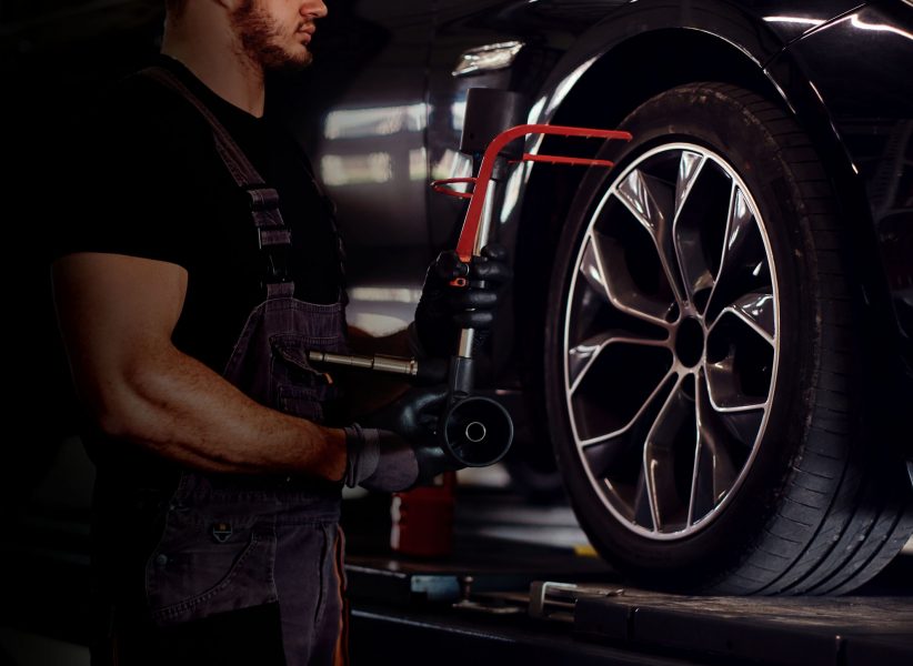 Muscular man is fixing car's wheel with special tool at auto service.
